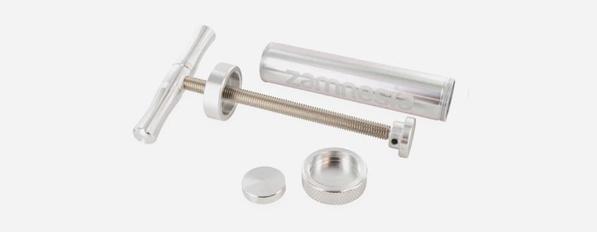 Zamnesia Super Pollen Press Een zilveren metalen spuit met een handvat en een zuiger.