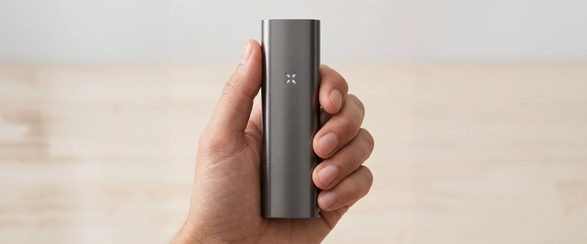 Productweergave van de PAX Four vaporizer in de hand PAX Four vaporizer vastgehouden in één hand, met zijn slanke matte behuizing, compacte formaat en led-bloembladindicator aan de voorkant