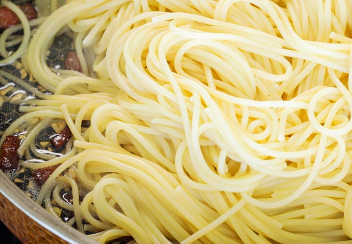 Uitgelekte spaghetti mengen met knapperige pancetta en geïnfuseerde boter in een pan, vierde stap voor cannabis-geïnfuseerde carbonara