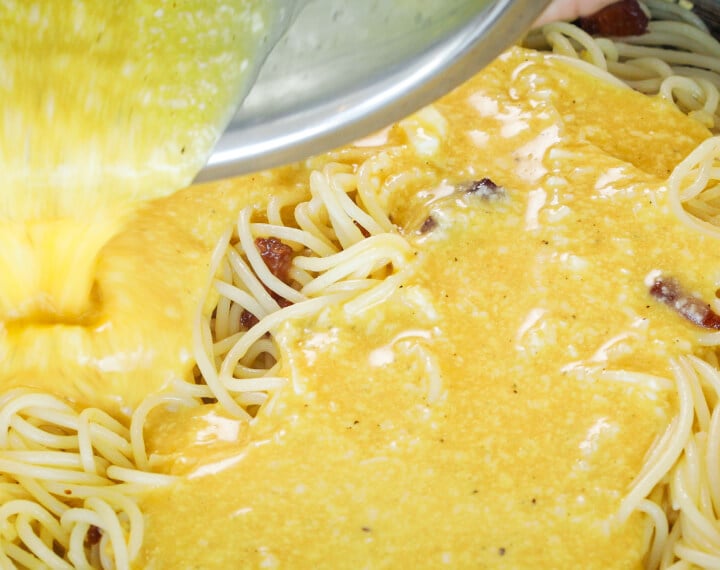 Eier- en kaasmengsel gieten over hete spaghetti in een pan, vijfde stap voor cannabis-geïnfuseerde carbonara